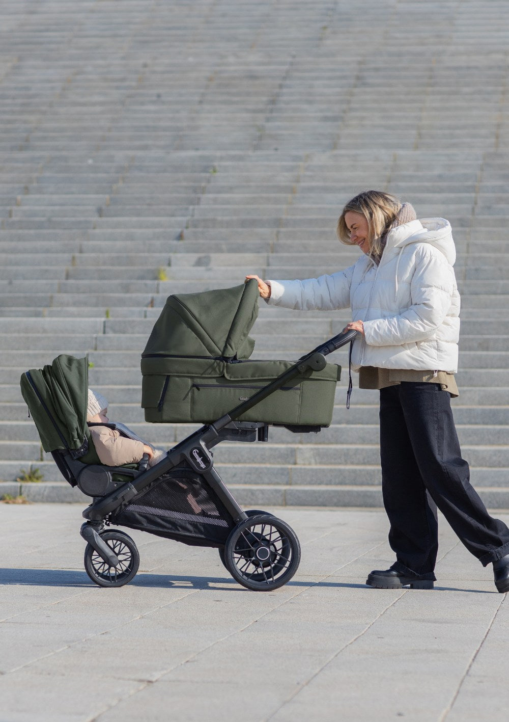 Frau schiebt zwei Kinder Emmaljunga Kinderwagen 'SENTO MAX ERGO+' Urban Green (Geschwistermodus)