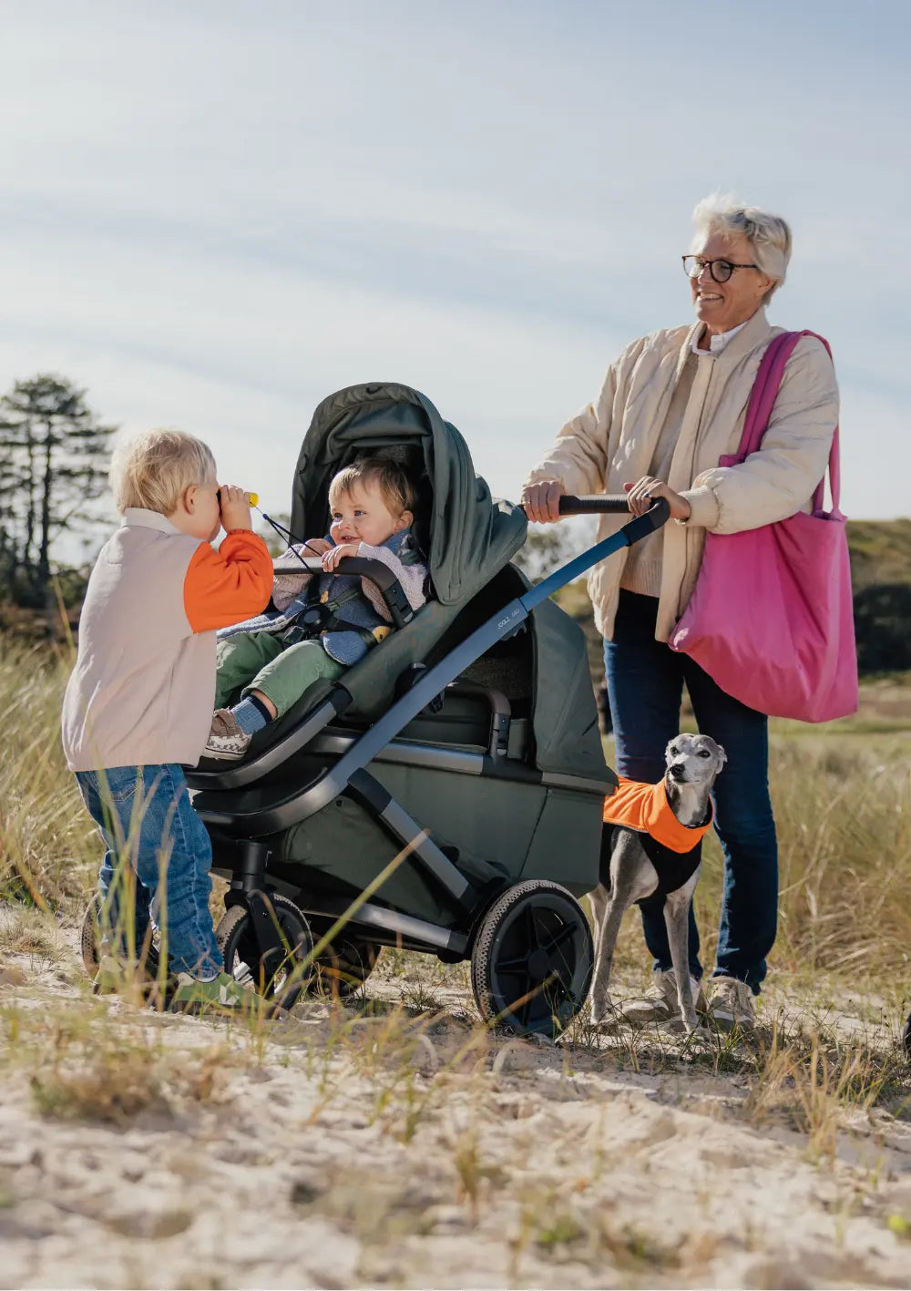 Frau schiebt den Joolz Geschwisterkinderwagen-Set 'Geo5 Double' Forest Green; ein Kind sitzt im Sportsitz, ein älteres Kind davor
